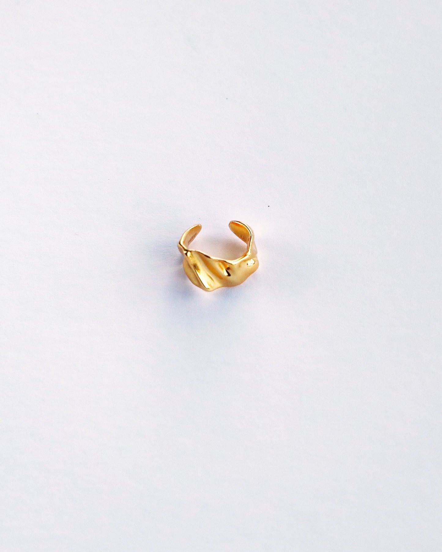 Top view of sculptural gold ear cuff on white background, highlighting wave texture