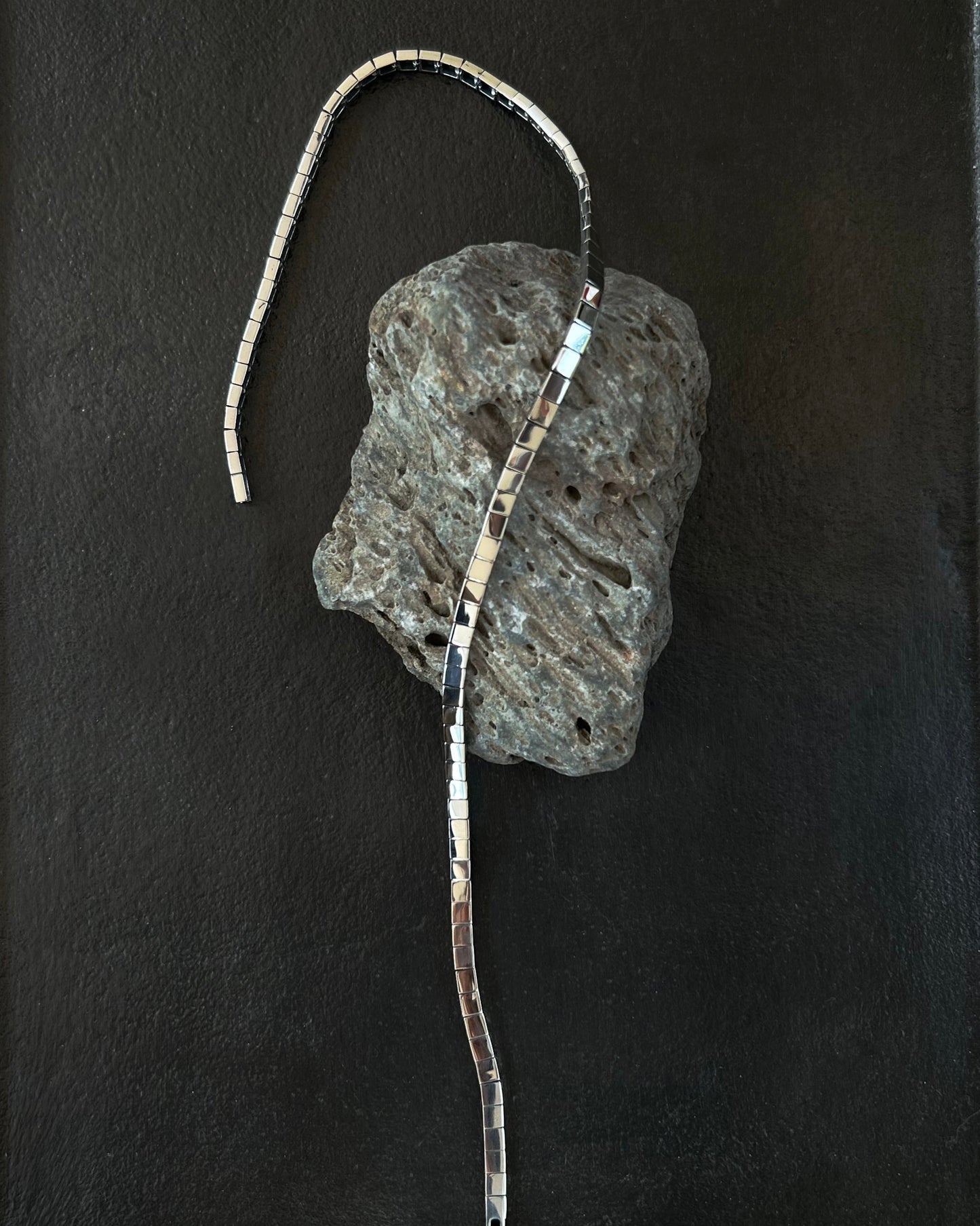 Minimalist silver necklace draped on volcanic stone and black tray display