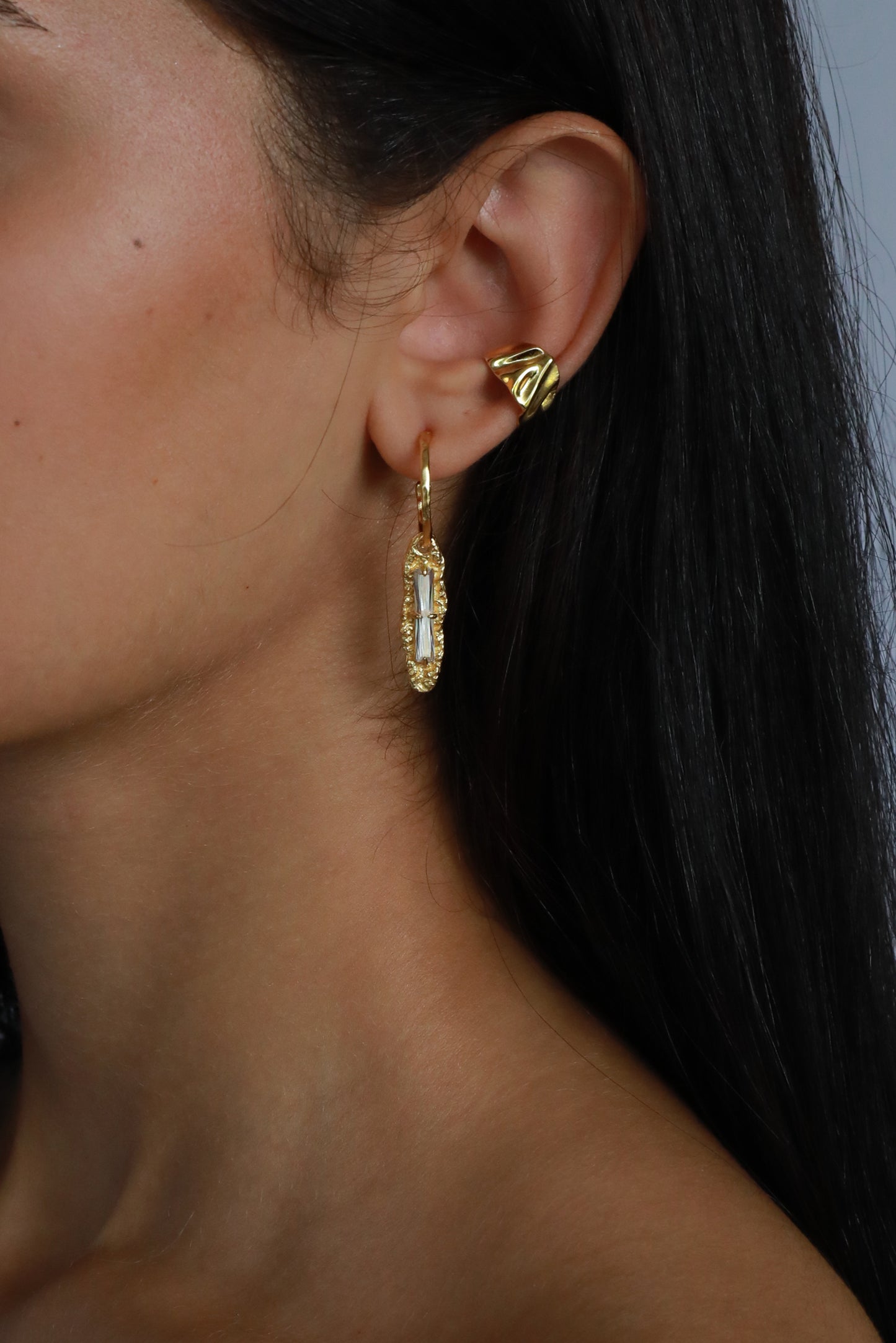 Close-up of 18k gold plated white zircon earring on model’s ear styled with gold ear cuff