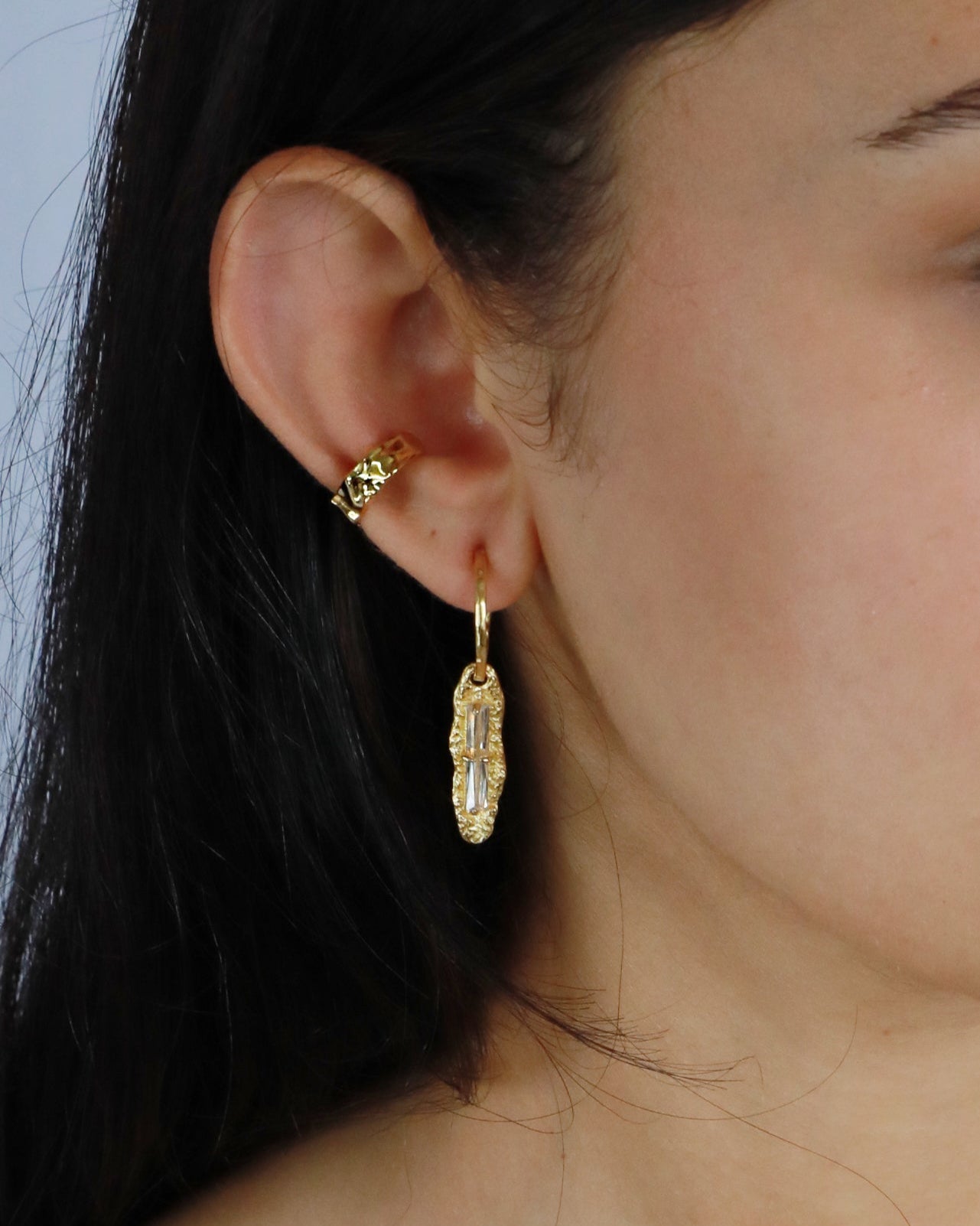 Model wearing gold sculpted ear cuff paired with silver hoop and rings, perfect stacked jewelry look