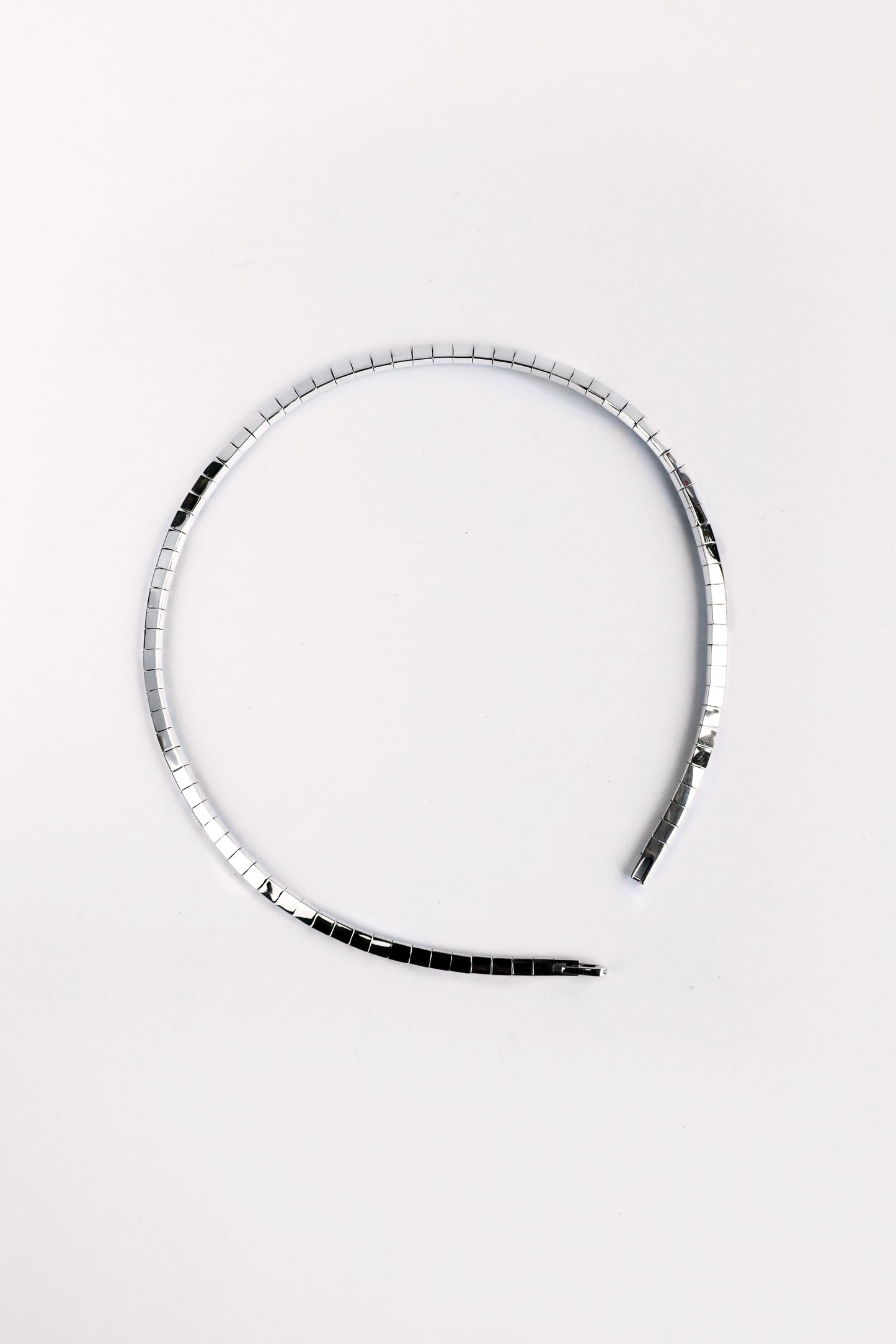 Flatlay of fluid sterling silver segmented necklace in circular shape on white background