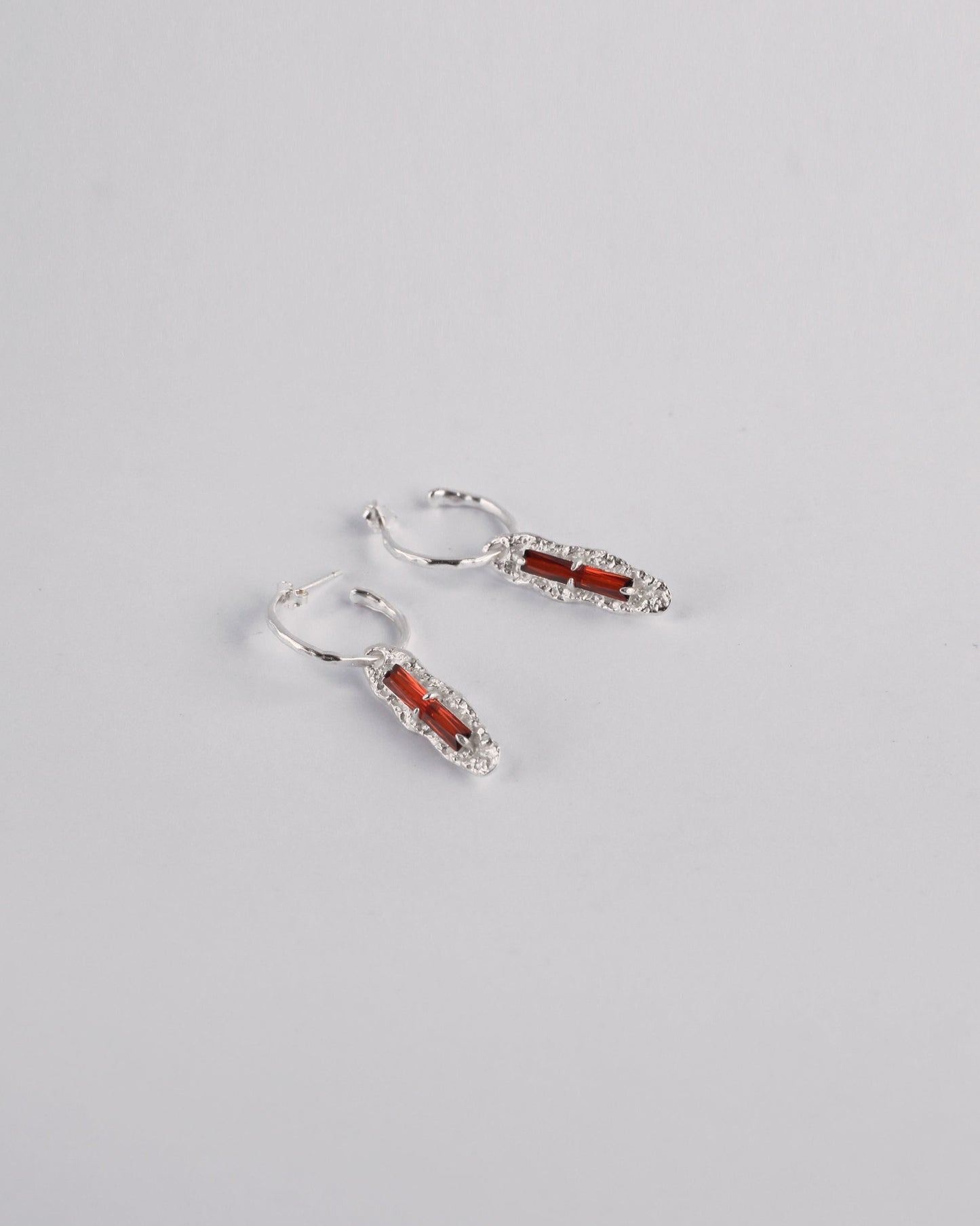 Angled view of red cubic zirconia earrings in sterling silver setting