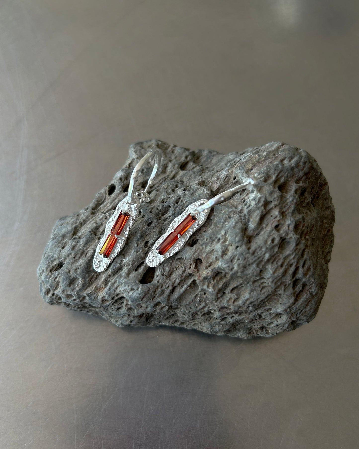 Detailed view of red zircon earrings displayed on lava rock