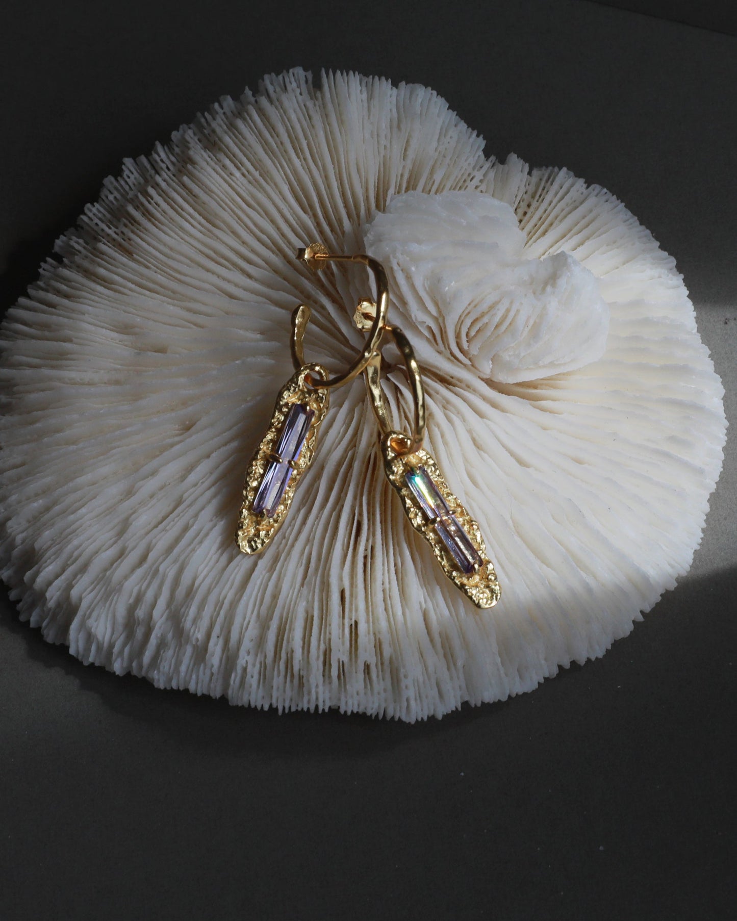 Twilight Gleam gold and purple zircon earrings styled on coral texture for jewelry photography