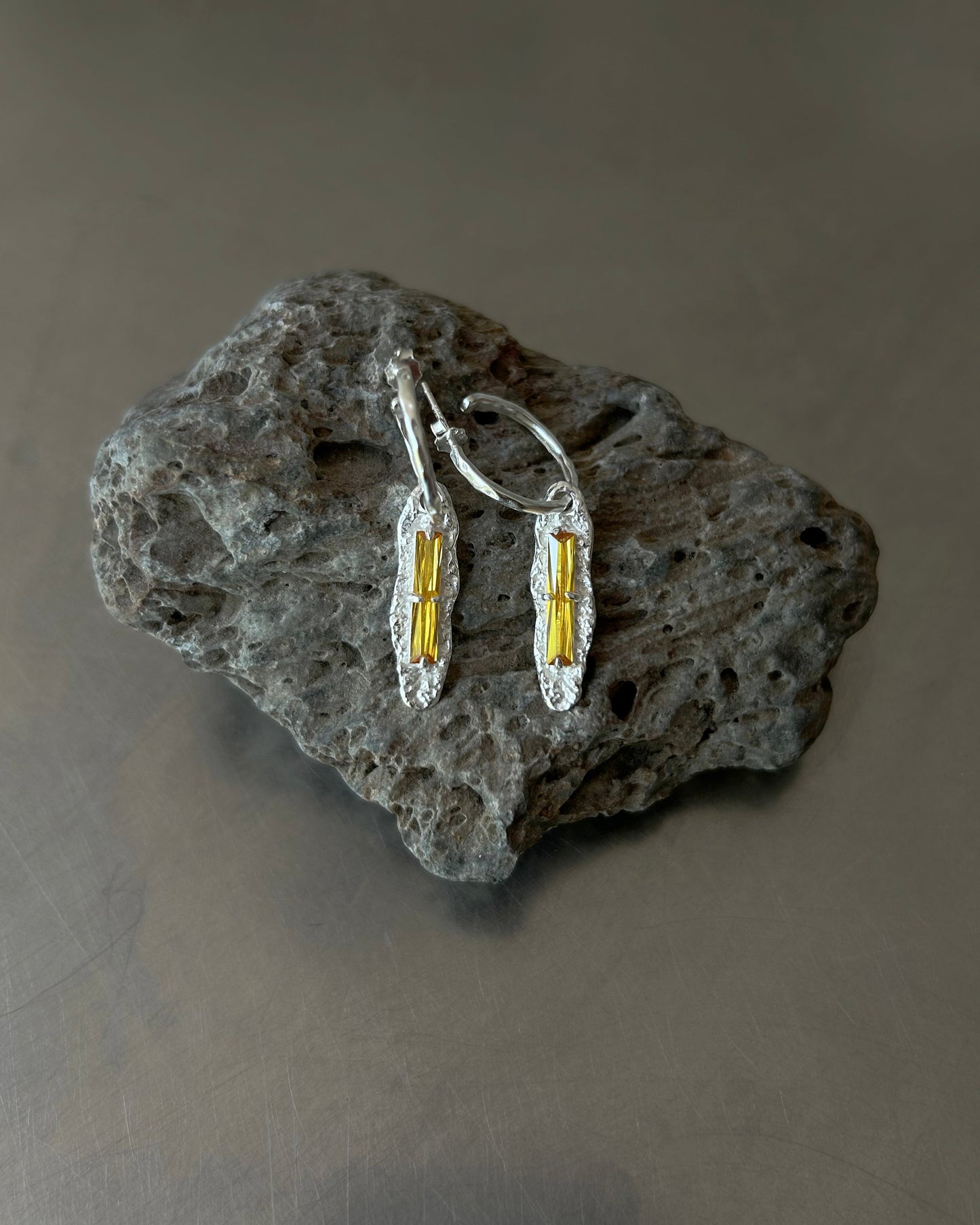 Yellow zircon drop earrings displayed on textured volcanic stone