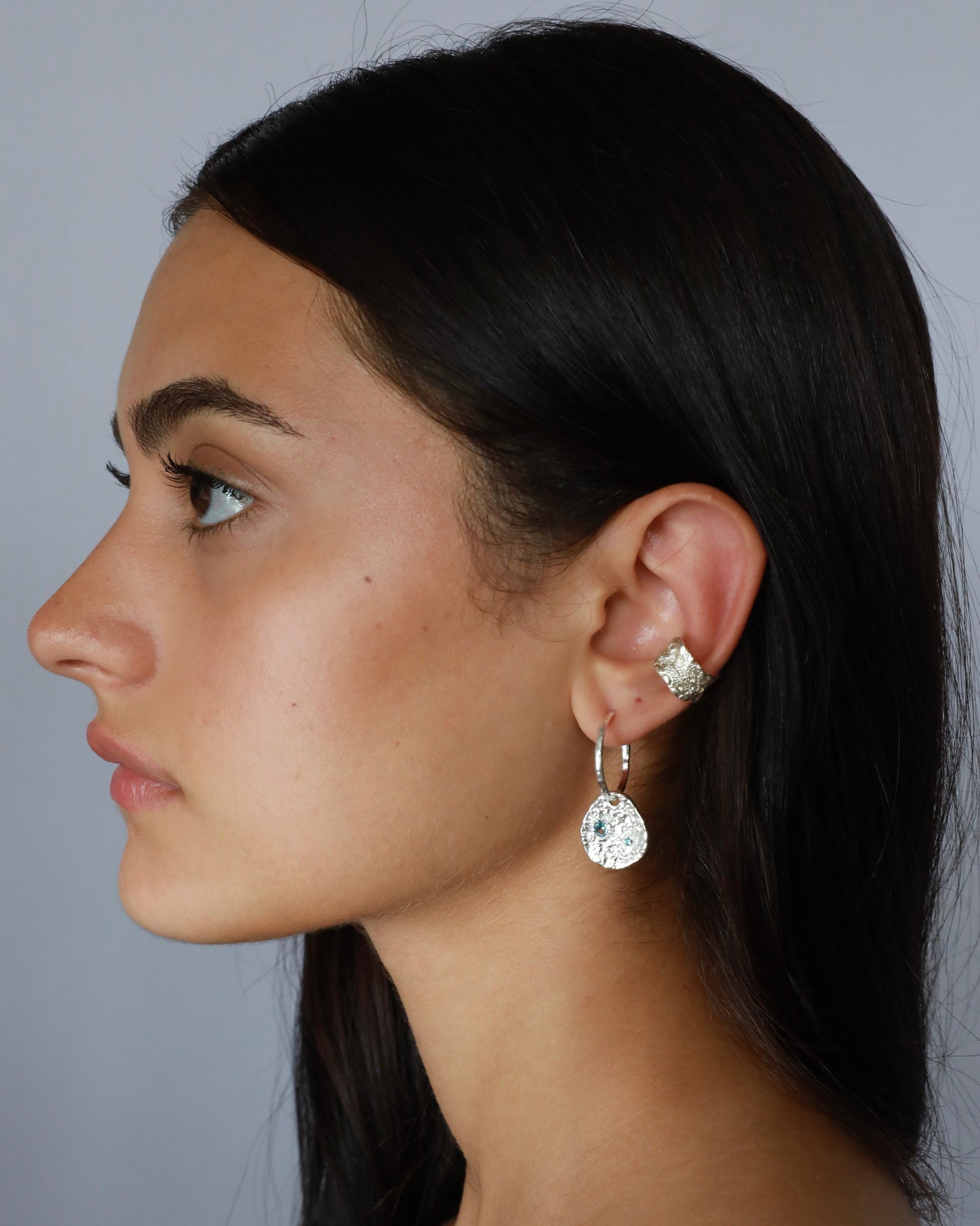 Silver coin drop earrings with hammered silver-plated brass pendants and two round lab-grown aquamarine-blue spinel stones on model