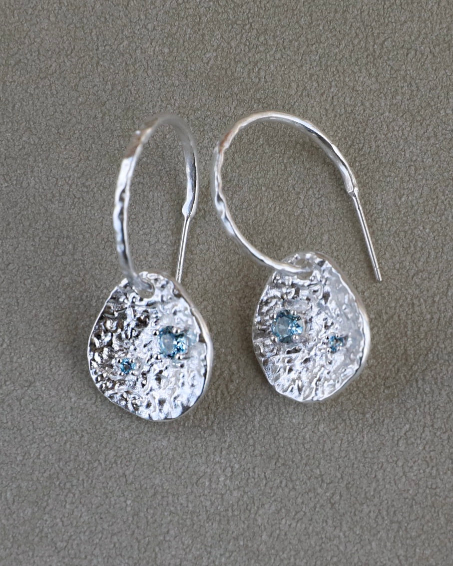 Silver coin drop earrings with hammered silver-plated brass pendants and two round lab-grown aquamarine-blue spinel stones.