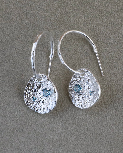 Silver coin drop earrings with hammered silver-plated brass pendants and two round lab-grown aquamarine-blue spinel stones.
