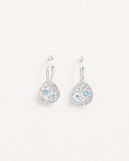 Silver coin drop earrings with hammered silver-plated brass pendants and two round lab-grown aquamarine-blue spinel stones.