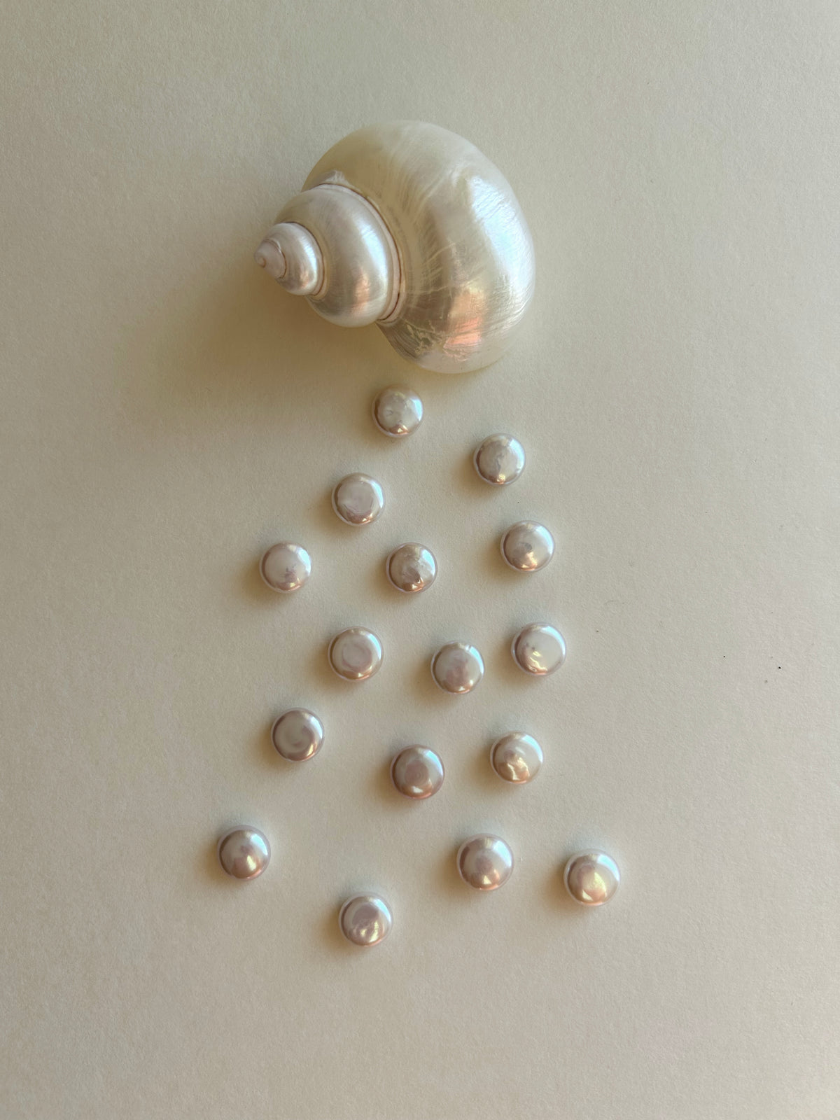 A natural pearl shell with several small, round, iridescent white pearls arranged below it on a plain beige background.