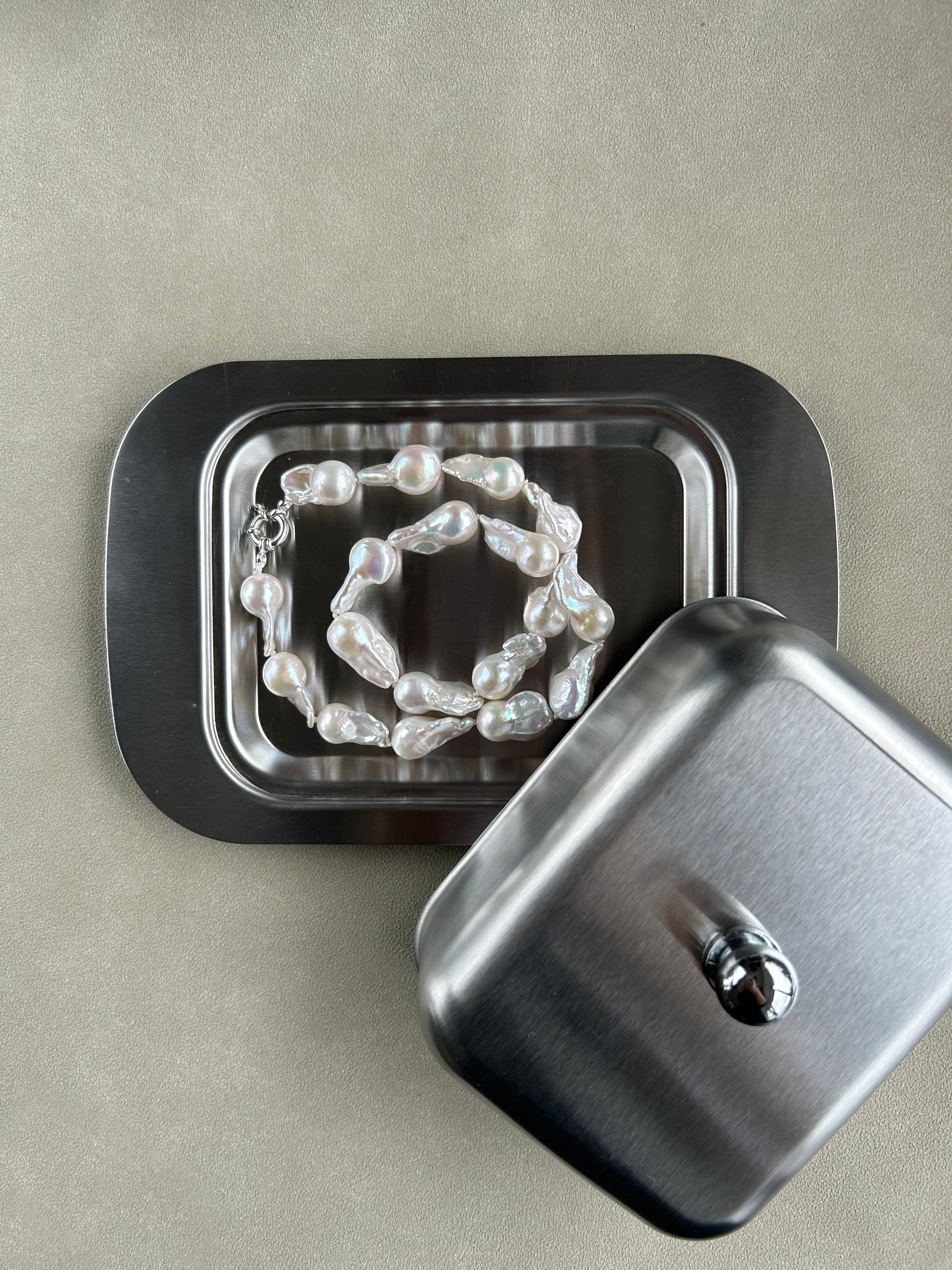 Pearl necklace inside a metal jewelry box on a beige background
