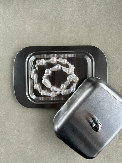 Pearl necklace inside a metal jewelry box on a beige background