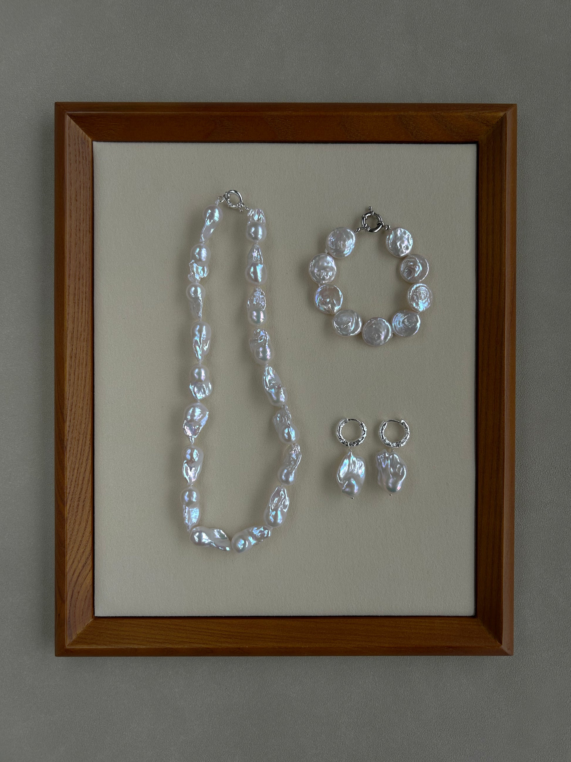 Jewelry set including a necklace, bracelet, and earrings in a wooden frame on a gray background