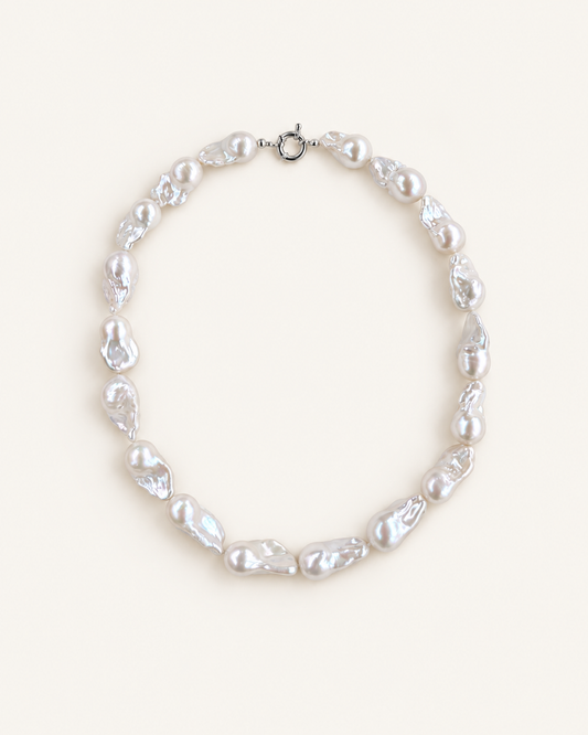 A baroque pearl necklace with irregular, organic-shaped white pearls and a silver lobster clasp, displayed on a clean, solid cream background.