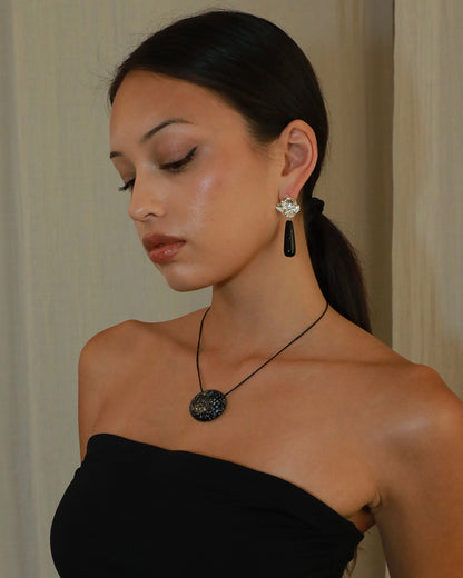 Silver-tone sculptural flower drop earrings with long polished black onyx stones on model