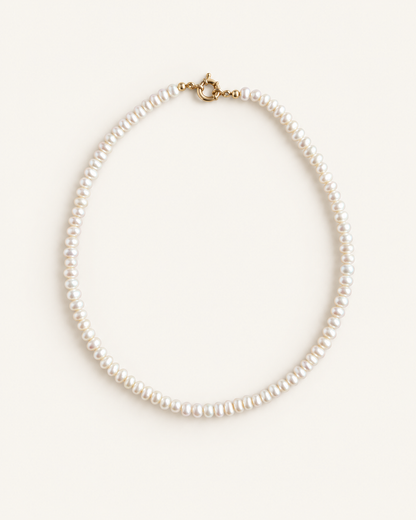 A classic pearl necklace with small, round white pearls and a gold clasp, displayed on a clean, light cream background.