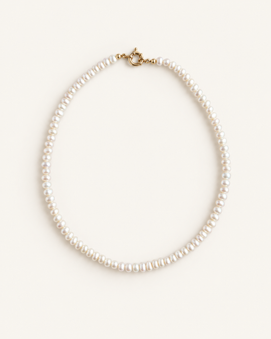 A classic pearl necklace with small, round white pearls and a gold clasp, displayed on a clean, light cream background.
