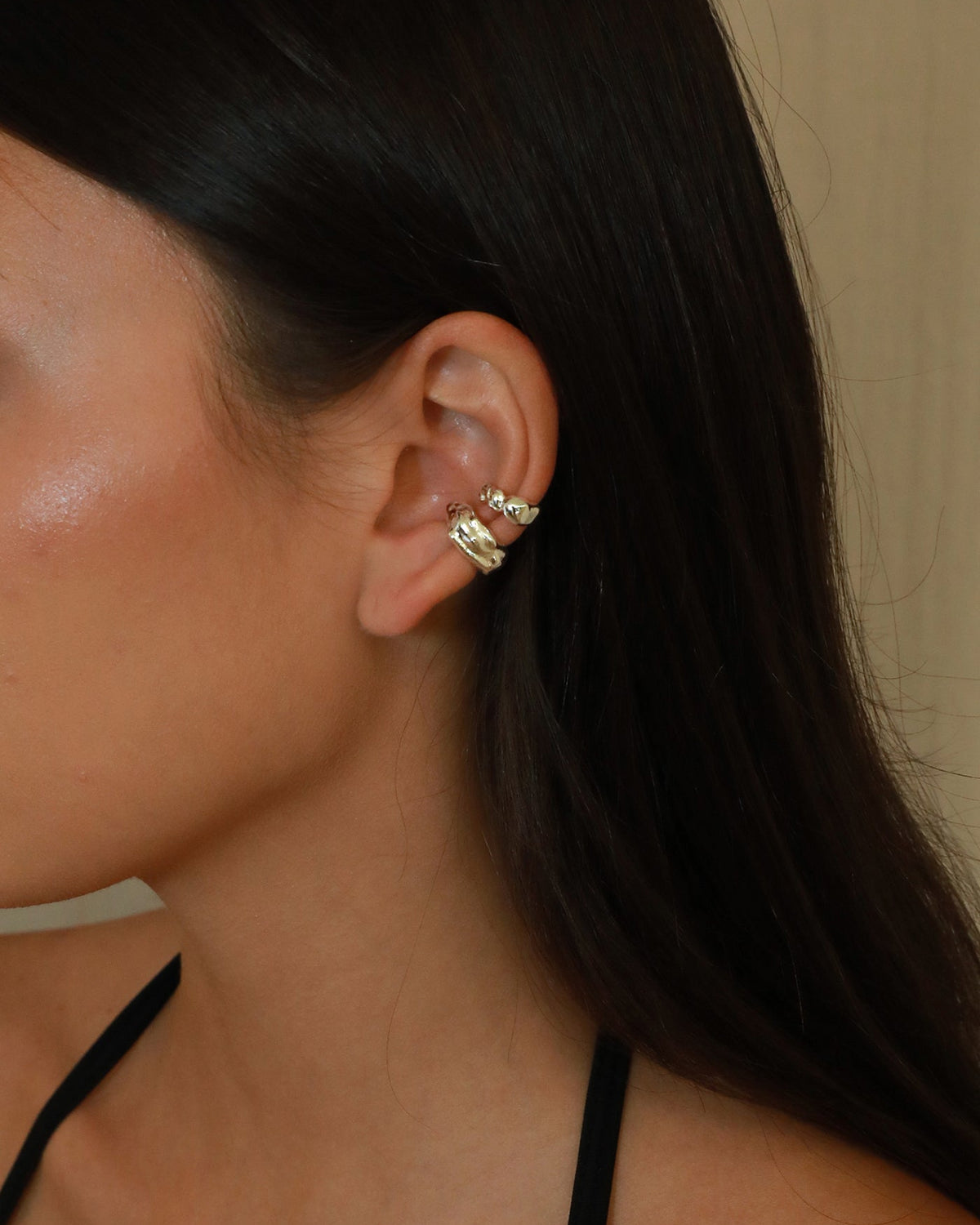 A close-up side profile of a woman with long dark hair wearing a pair of stacked silver earcuff on her ear.