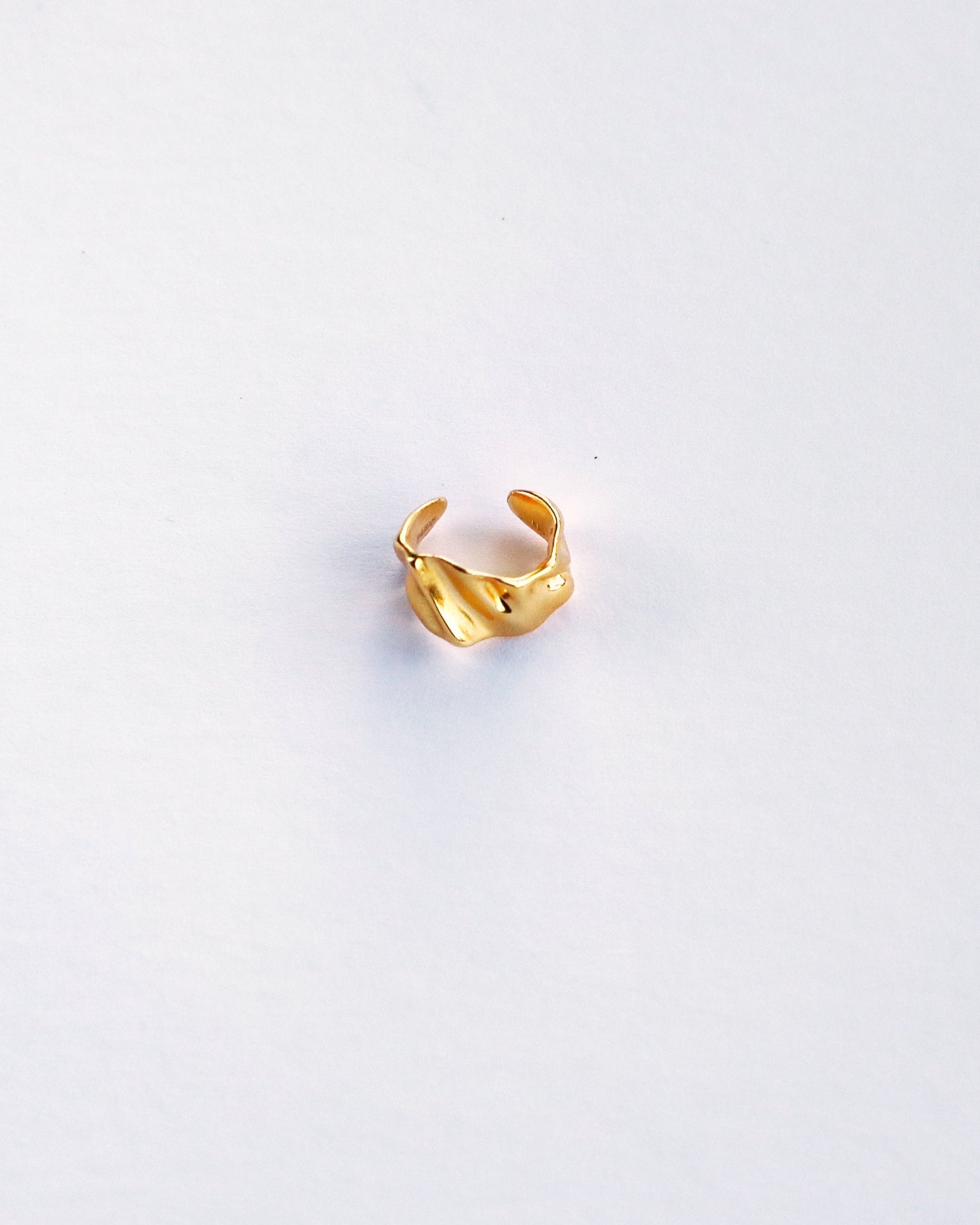 Top view of sculptural gold ear cuff on white background, highlighting wave texture