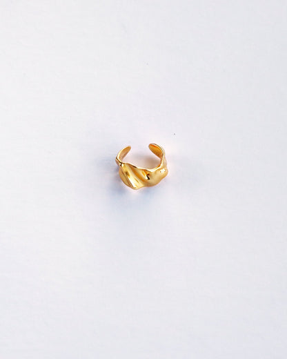 Top view of sculptural gold ear cuff on white background, highlighting wave texture