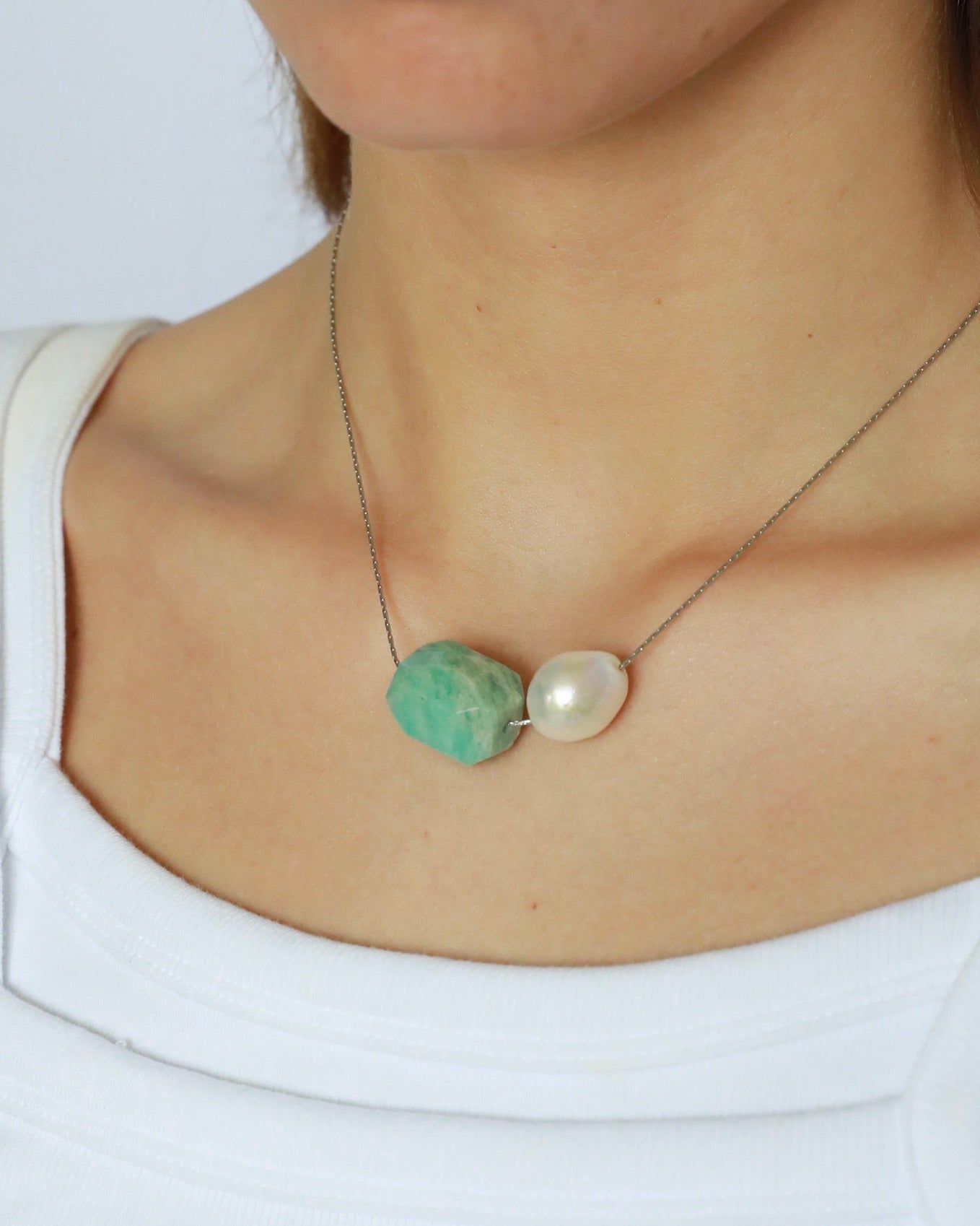 Necklace with a green stone and pearl pendant on a white background