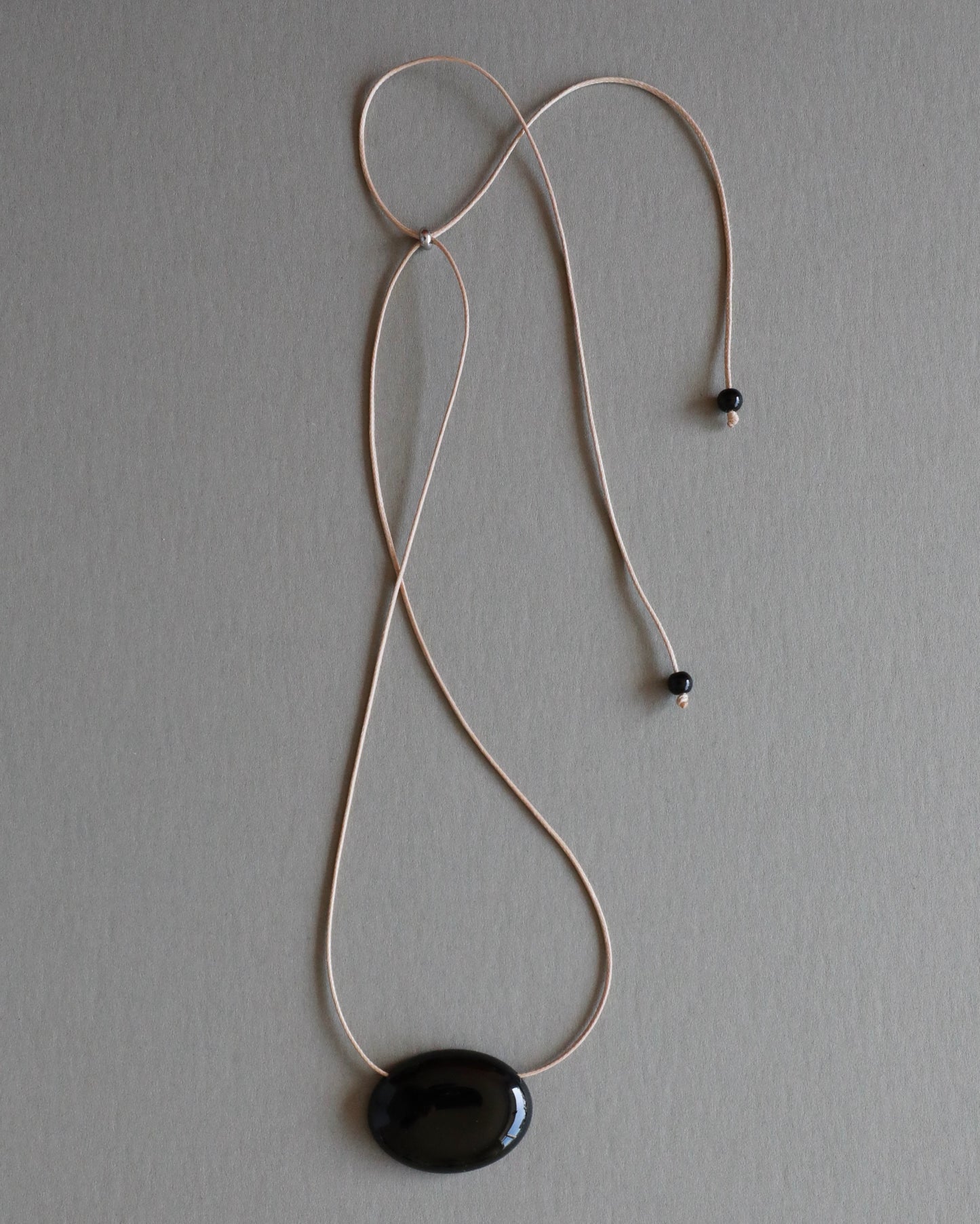 Super long adjustable necklace with polished natural black onyx pendant on soft beige cord. Minimal modern natural stone jewelry.
