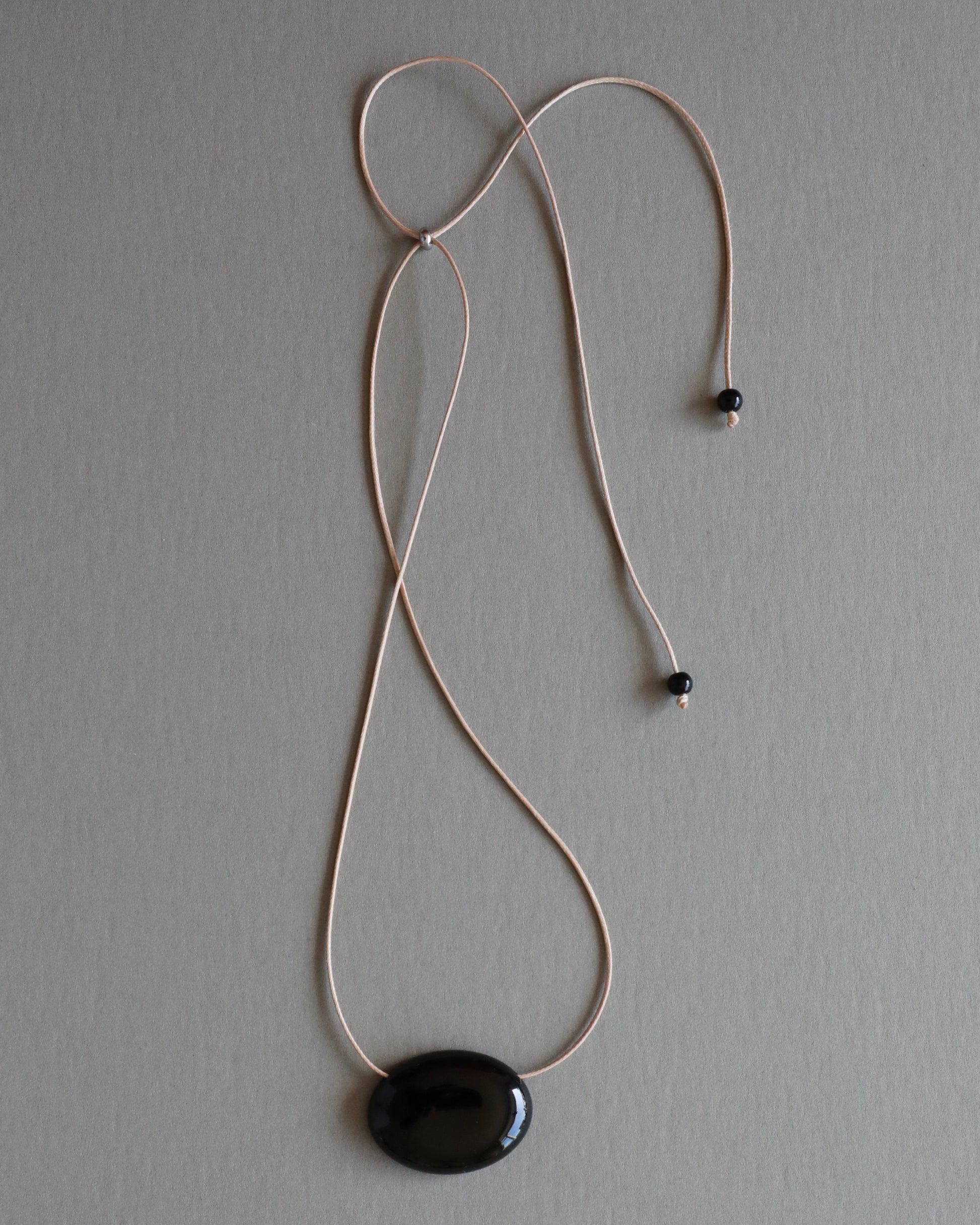 Super long adjustable necklace with polished natural black onyx pendant on soft beige cord. Minimal modern natural stone jewelry.