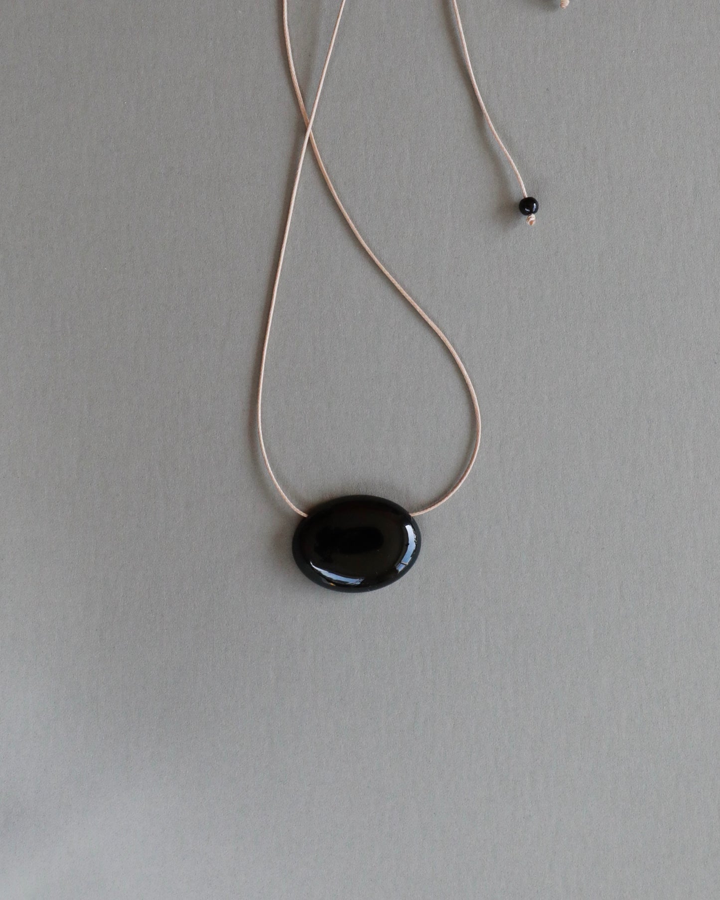Super long adjustable necklace with polished natural black onyx pendant on soft beige cord. Minimal modern natural stone jewellery