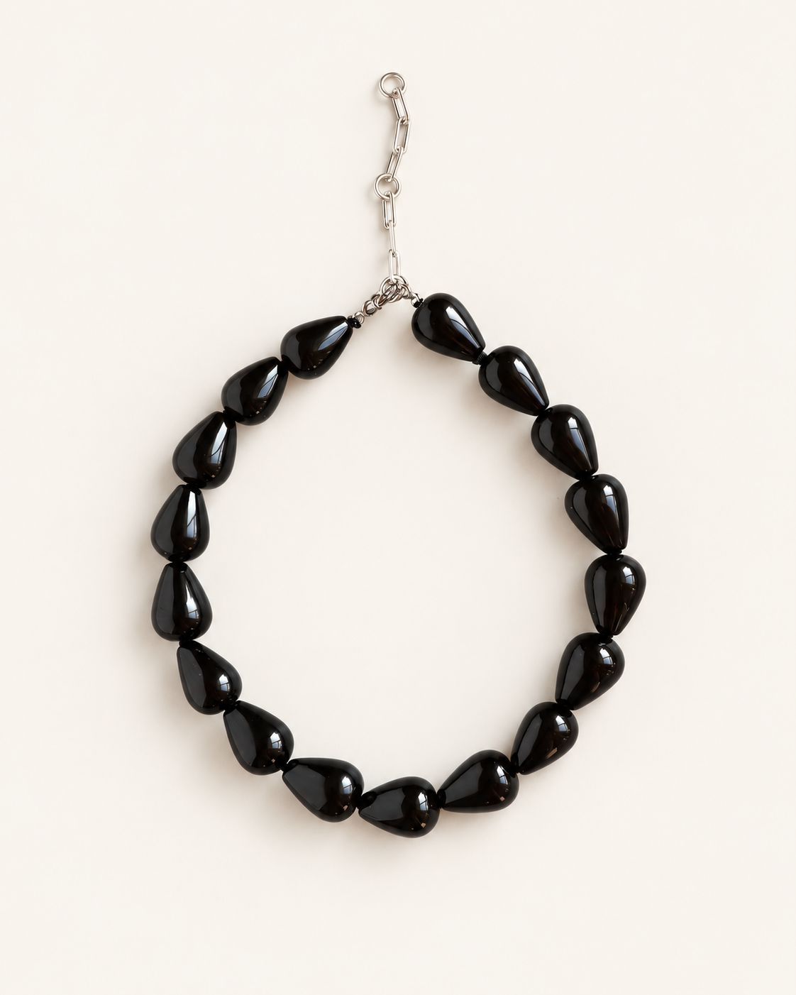 A beaded necklace made of glossy black teardrop-shaped beads with a silver-tone clasp, displayed on a light cream background.