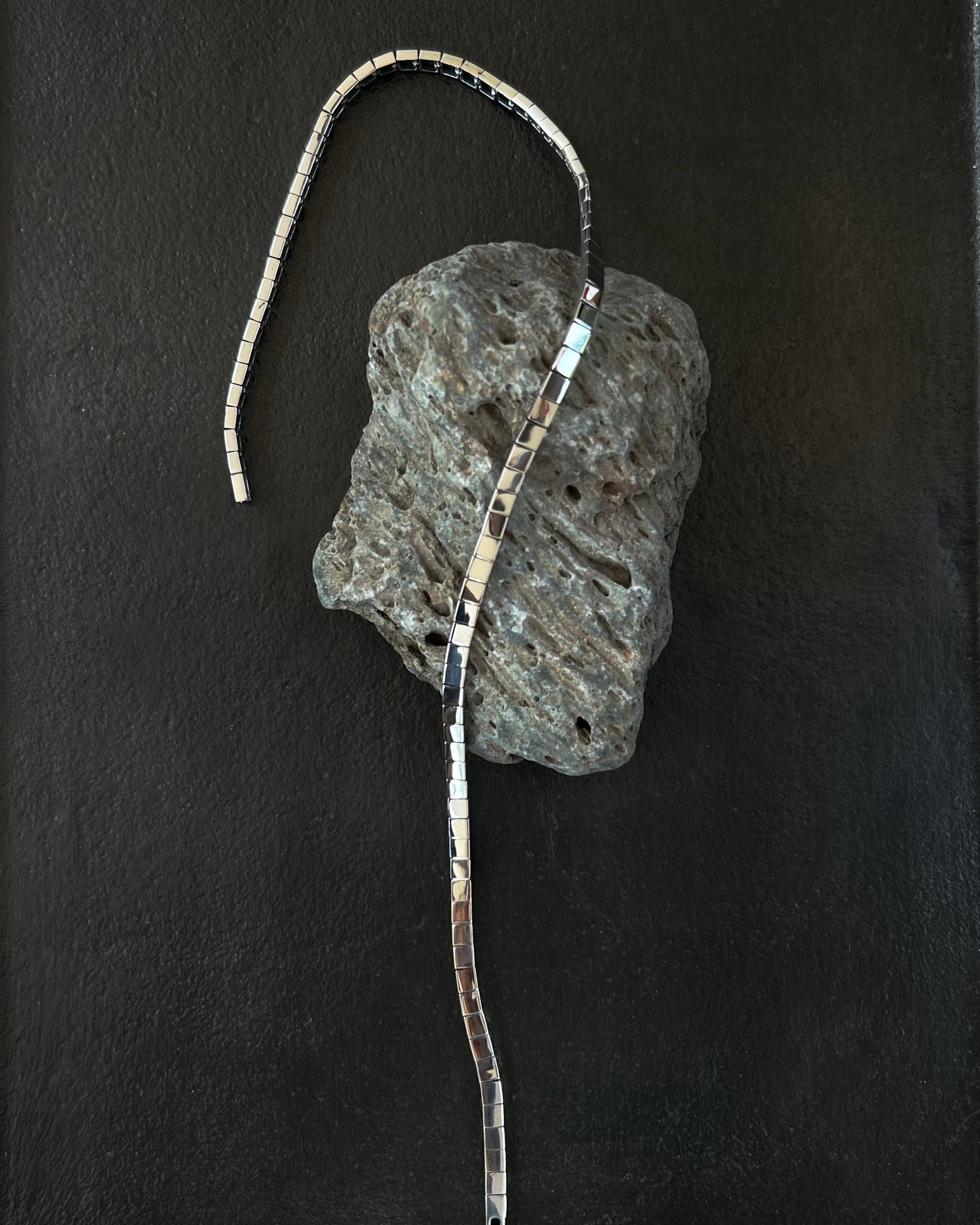 Minimalist silver necklace draped on volcanic stone and black tray display