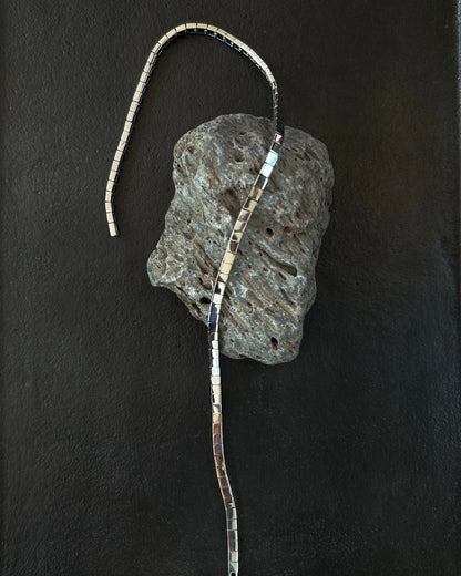 Minimalist silver necklace draped on volcanic stone and black tray display