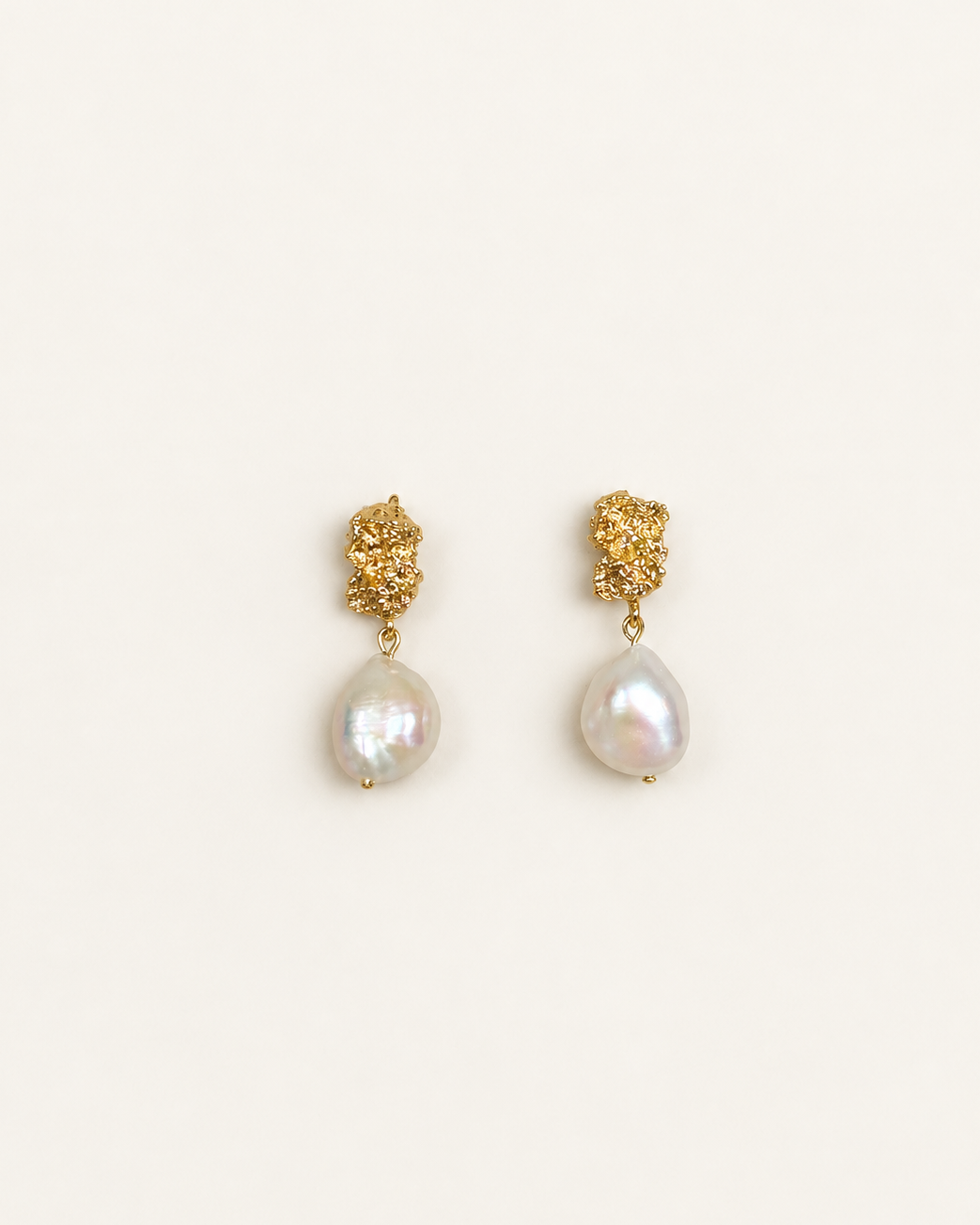 A pair of gold dangle earrings featuring textured gold studs and teardrop-shaped white baroque pearls, displayed on a clean off-white background.