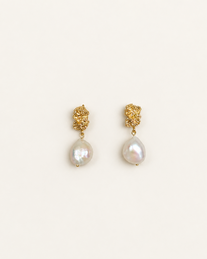 A pair of gold dangle earrings featuring textured gold studs and teardrop-shaped white baroque pearls, displayed on a clean off-white background.