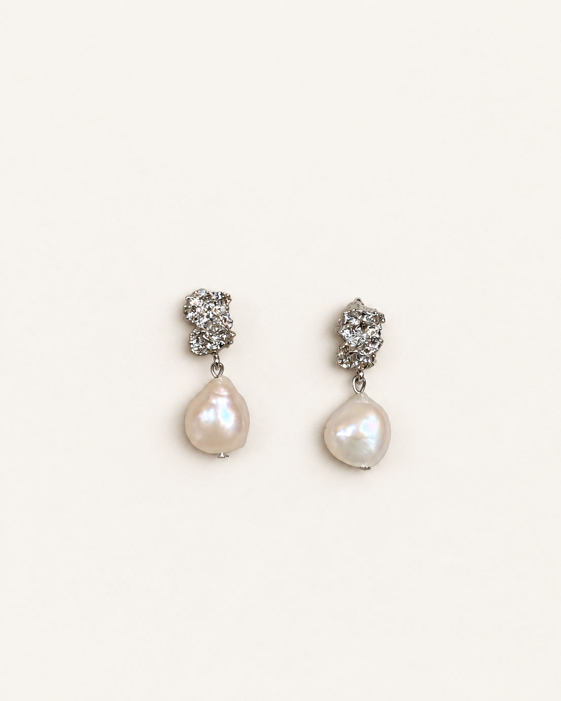 A pair of silver-toned drop earrings featuring a textured hoop at the top and a teardrop-shaped white baroque pearl hanging below, set against a plain off-white background.