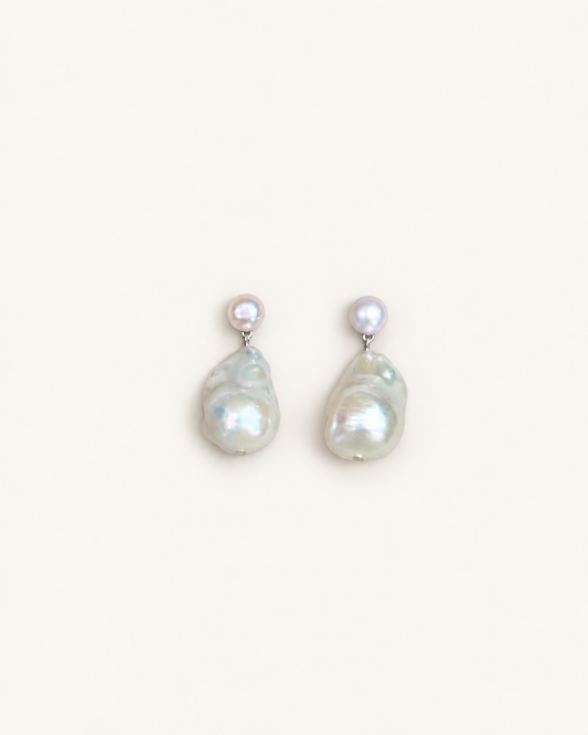 A pair of baroque pearl drop earrings with small round pearl studs on silver-toned posts, displayed against a solid off-white background.