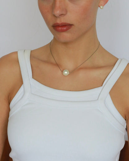 Woman wearing a white tank top and pearl necklace against a plain background