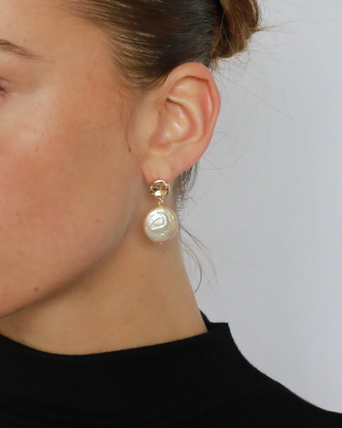 Close-up of a person wearing pearl earrings with a plain background