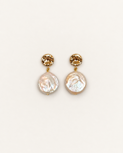 A pair of gold drop earrings featuring a faceted round gold top and a hanging irregular baroque pearl, shown on a plain off-white background.