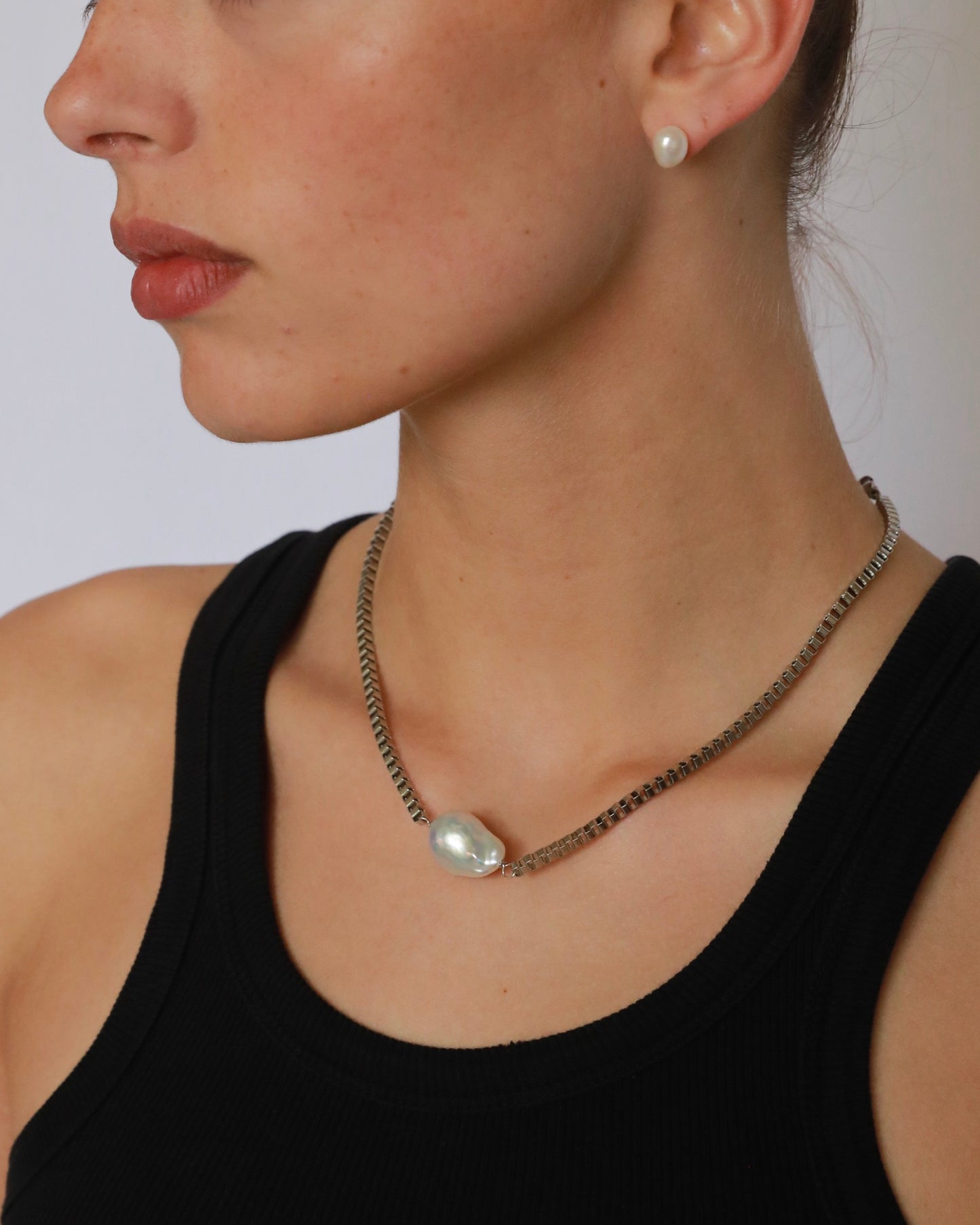 Close-up of a woman wearing a pearl necklace and earrings against a neutral background