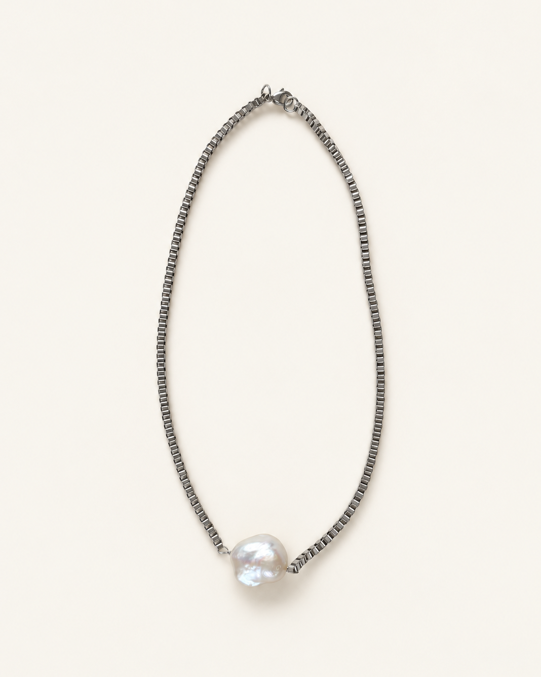 A delicate silver-toned beaded chain necklace with a single large, lustrous white baroque pearl pendant, displayed on a clean, solid off-white background.