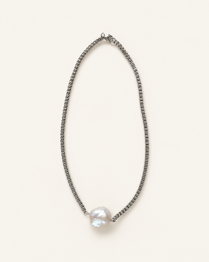 A delicate silver-toned beaded chain necklace with a single large, lustrous white baroque pearl pendant, displayed on a clean, solid off-white background.