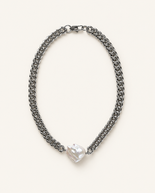 A stainless chain necklace with a single irregular, lustrous white pearl pendant, displayed on a clean off-white background.