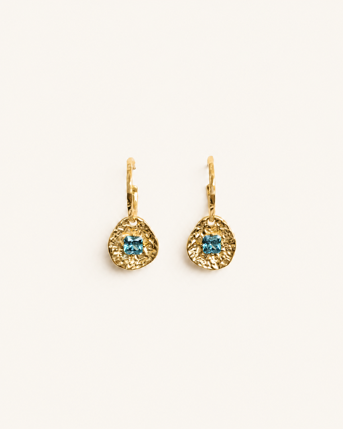 Cleo gold-plated brass coin drop earrings with hammered texture and square blue tourmaline CZ stones on a soft white background.