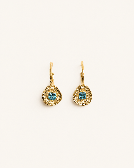 Cleo gold-plated brass coin drop earrings with hammered texture and square blue tourmaline CZ stones on a soft white background.