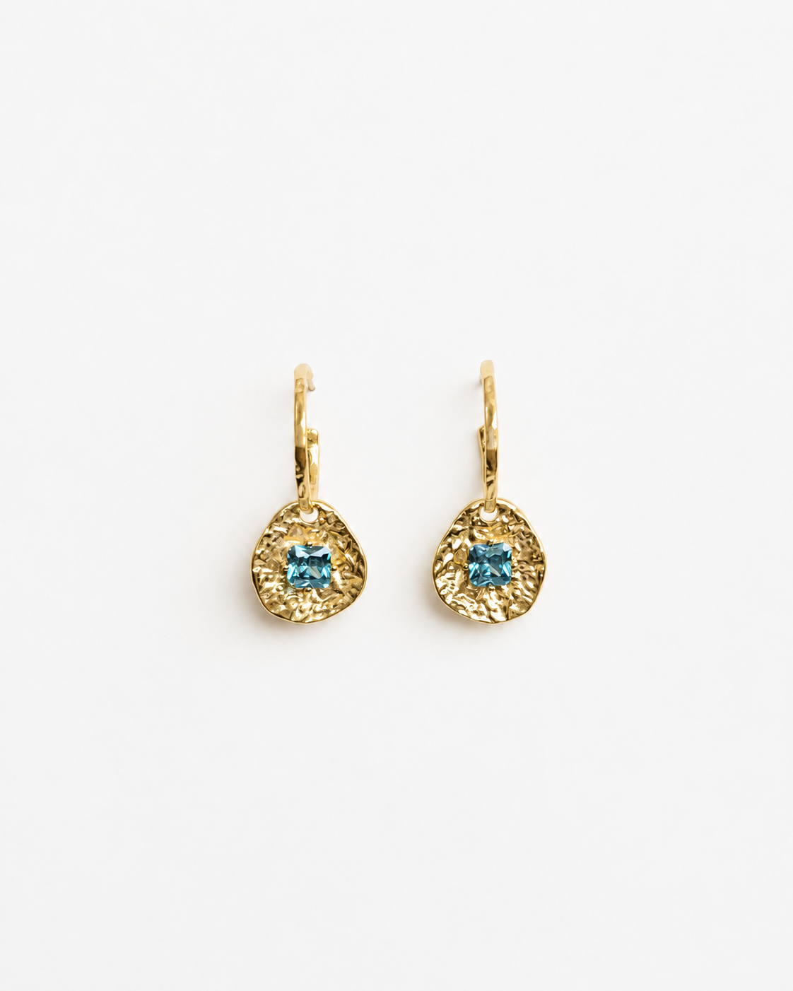 Cleo gold-plated brass coin drop earrings with hammered texture and square blue tourmaline CZ stones on a soft white background.