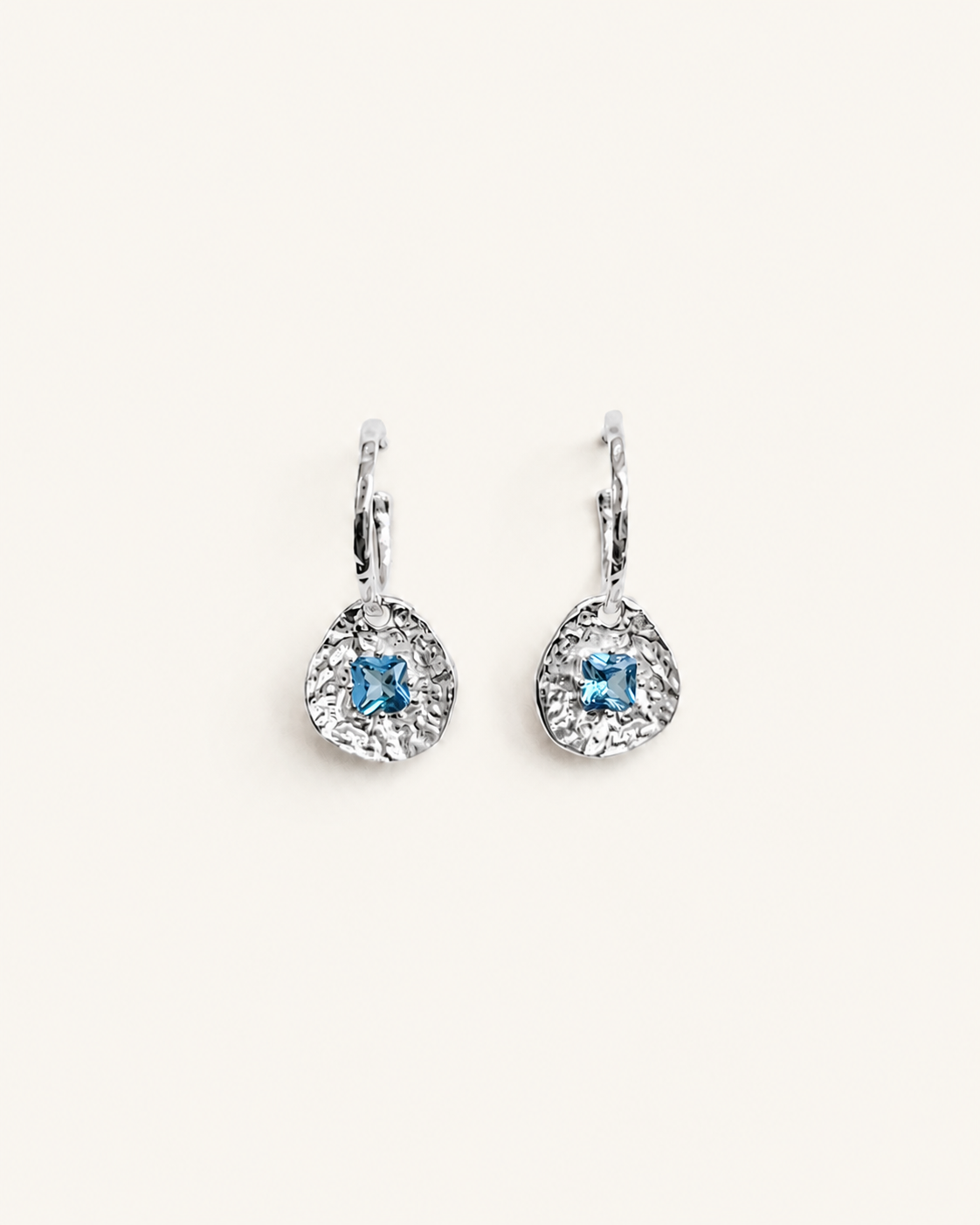 Cleo silver-plated brass coin drop earrings with hammered texture and square blue tourmaline CZ stones on a soft white background.