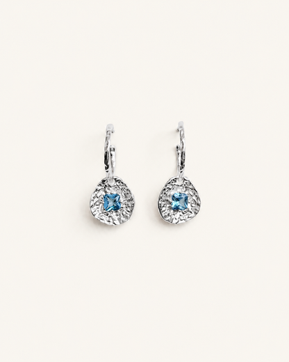 Cleo silver-plated brass coin drop earrings with hammered texture and square blue tourmaline CZ stones on a soft white background.
