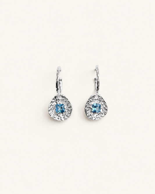Cleo silver-plated brass coin drop earrings with hammered texture and square blue tourmaline CZ stones on a soft white background.