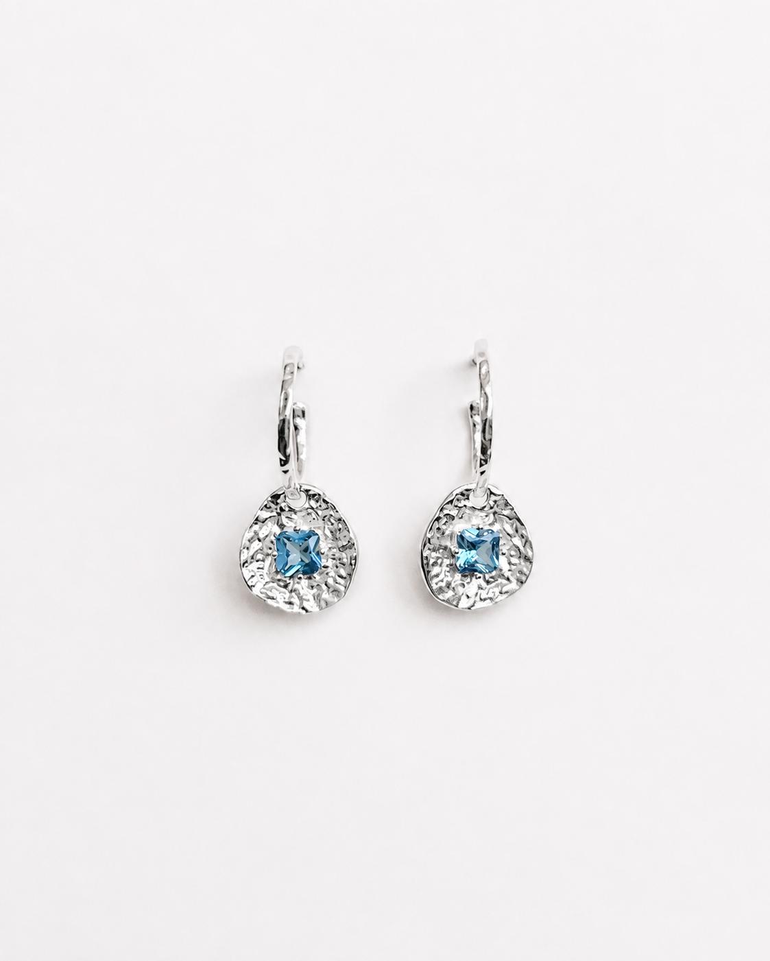 Cleo silver-plated brass coin drop earrings with hammered texture and square blue tourmaline CZ stones on a soft white background.