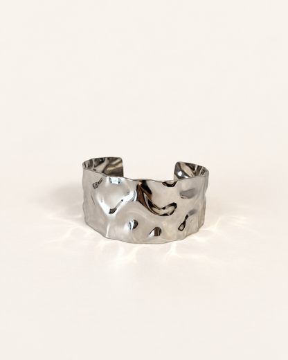 A hammered silver cuff bracelet with an organic, textured surface, photographed on a clean off-white background.